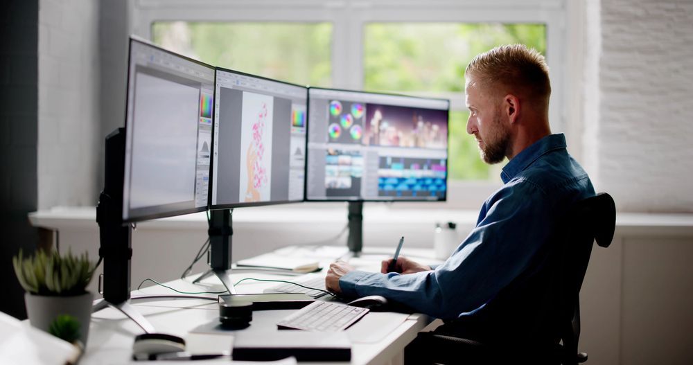 A man is sitting at a desk in front of three computer monitors.
