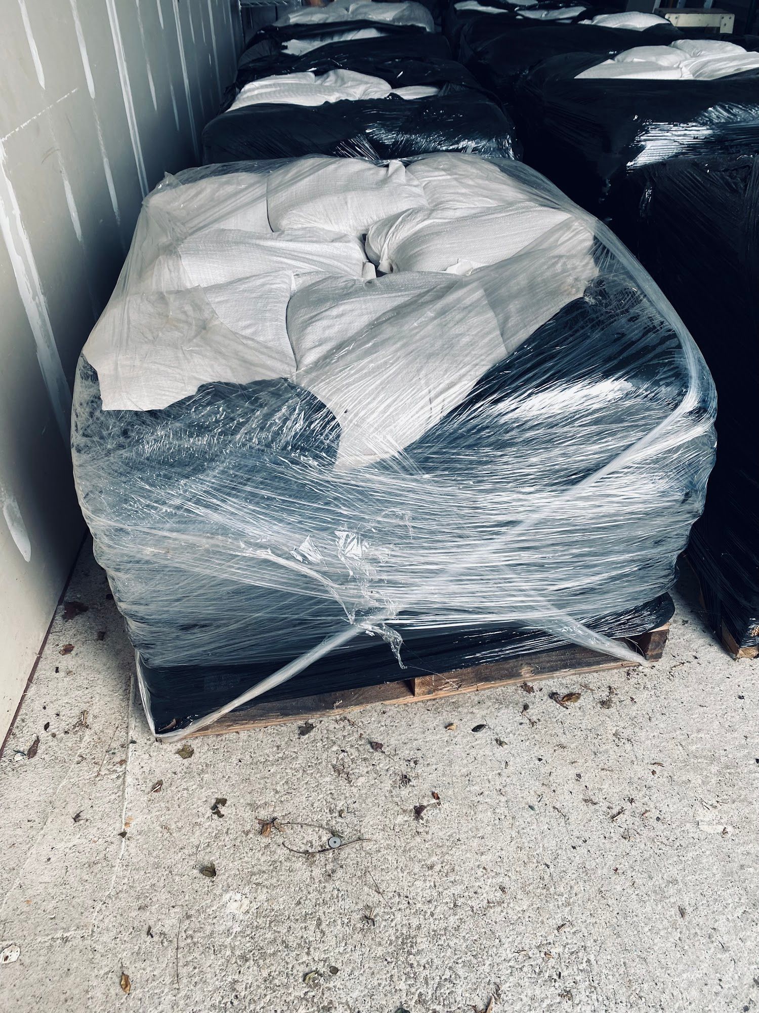 Pallet wrapped in plastic with a white cover, sitting in a storage area with debris on the floor