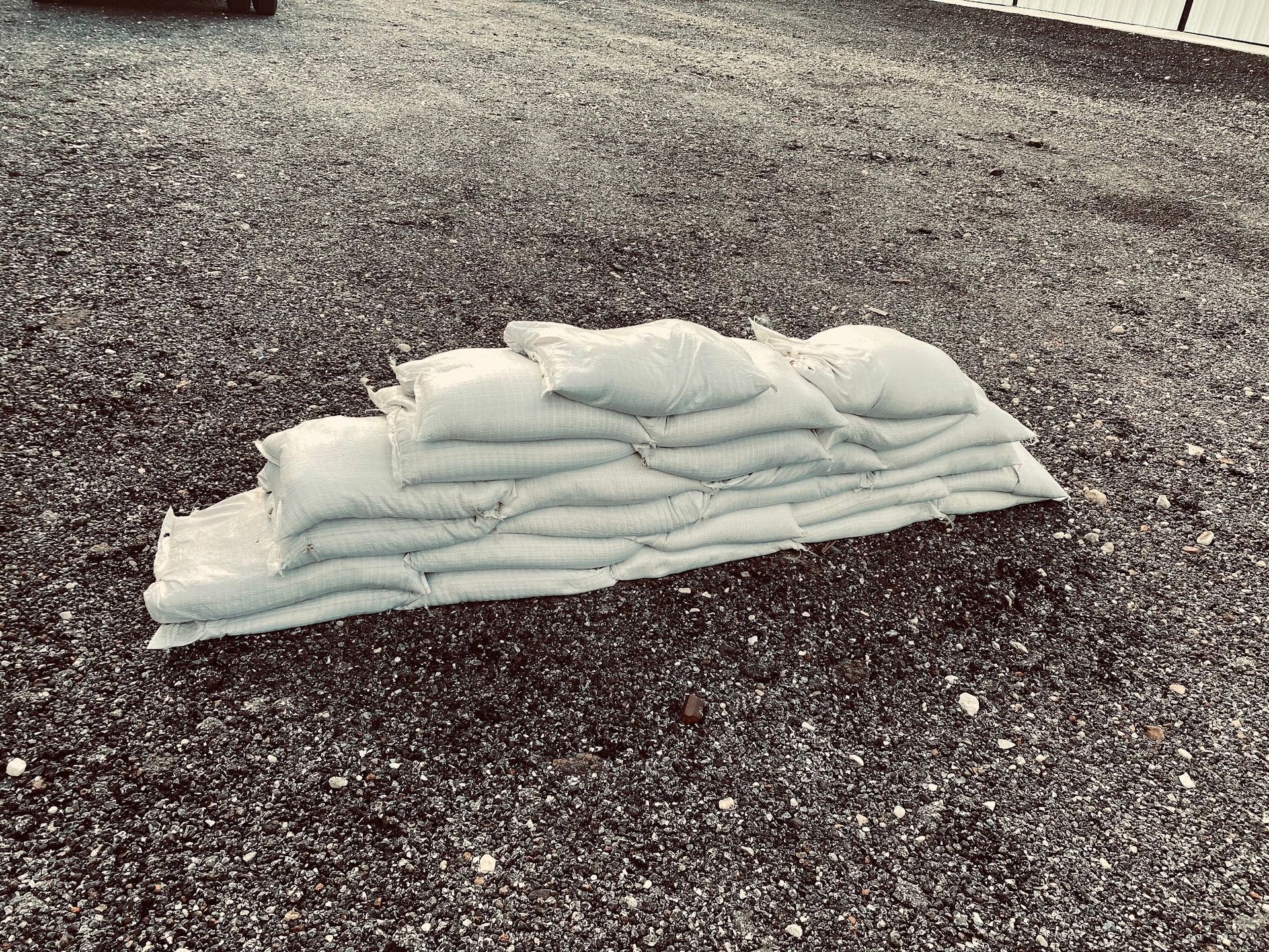 Stack of white sandbags on a gravel surface outdoors.