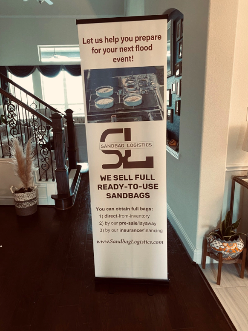 Tall banner for self-serve ready-to-use sandwich station in a lobby, beside a staircase and plants.