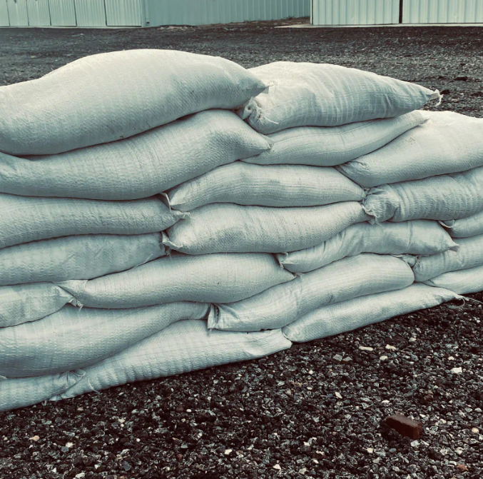 Stacked white sandbags along a gravel surface near a building wall
