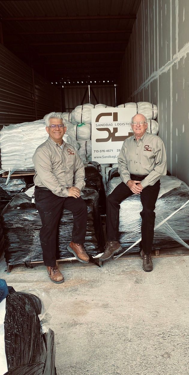 Stacked white and black bags in a warehouse, with a pallet sign marked “SL” in the background