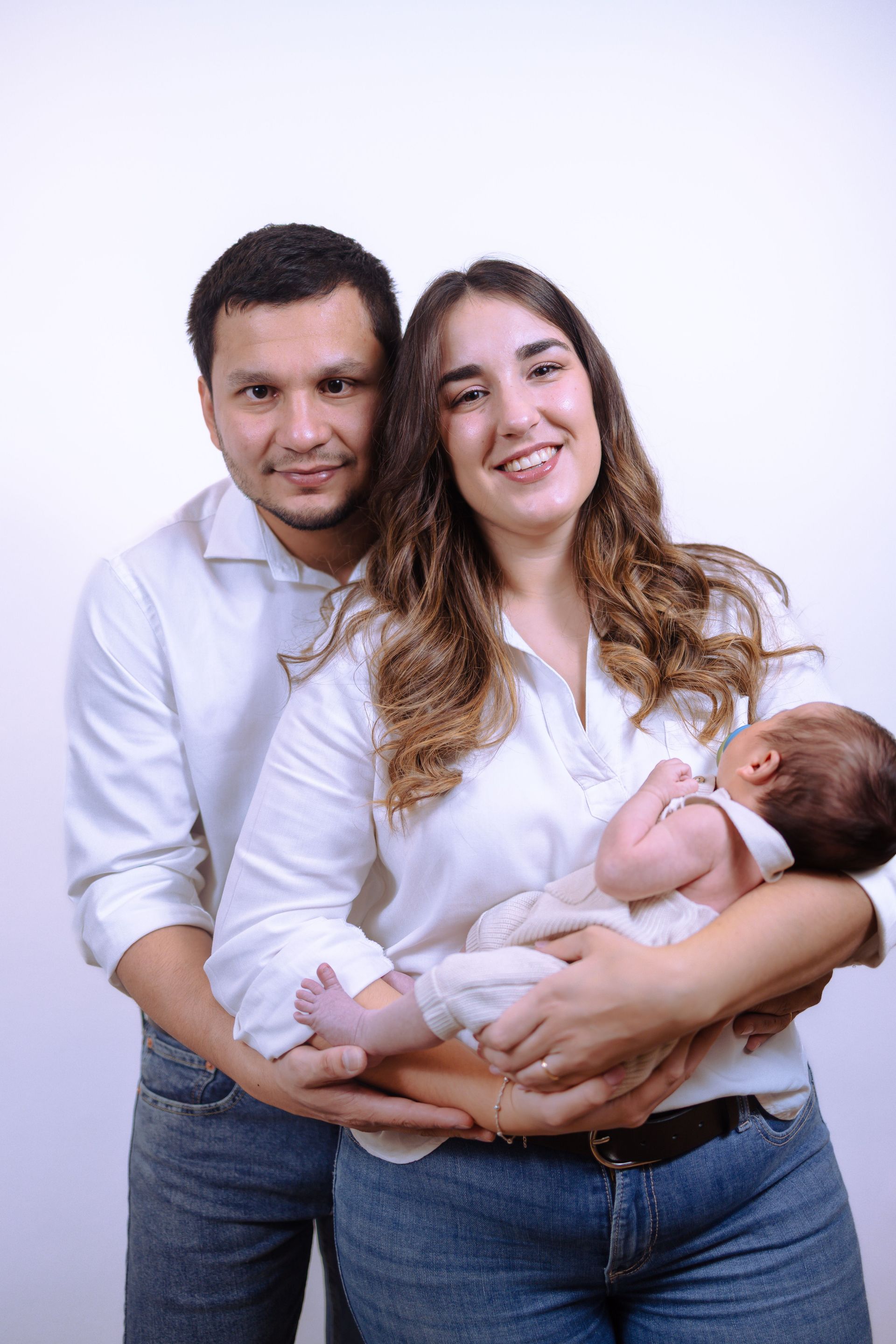 Family portrait of two adults holding a sleeping baby against a white backdrop