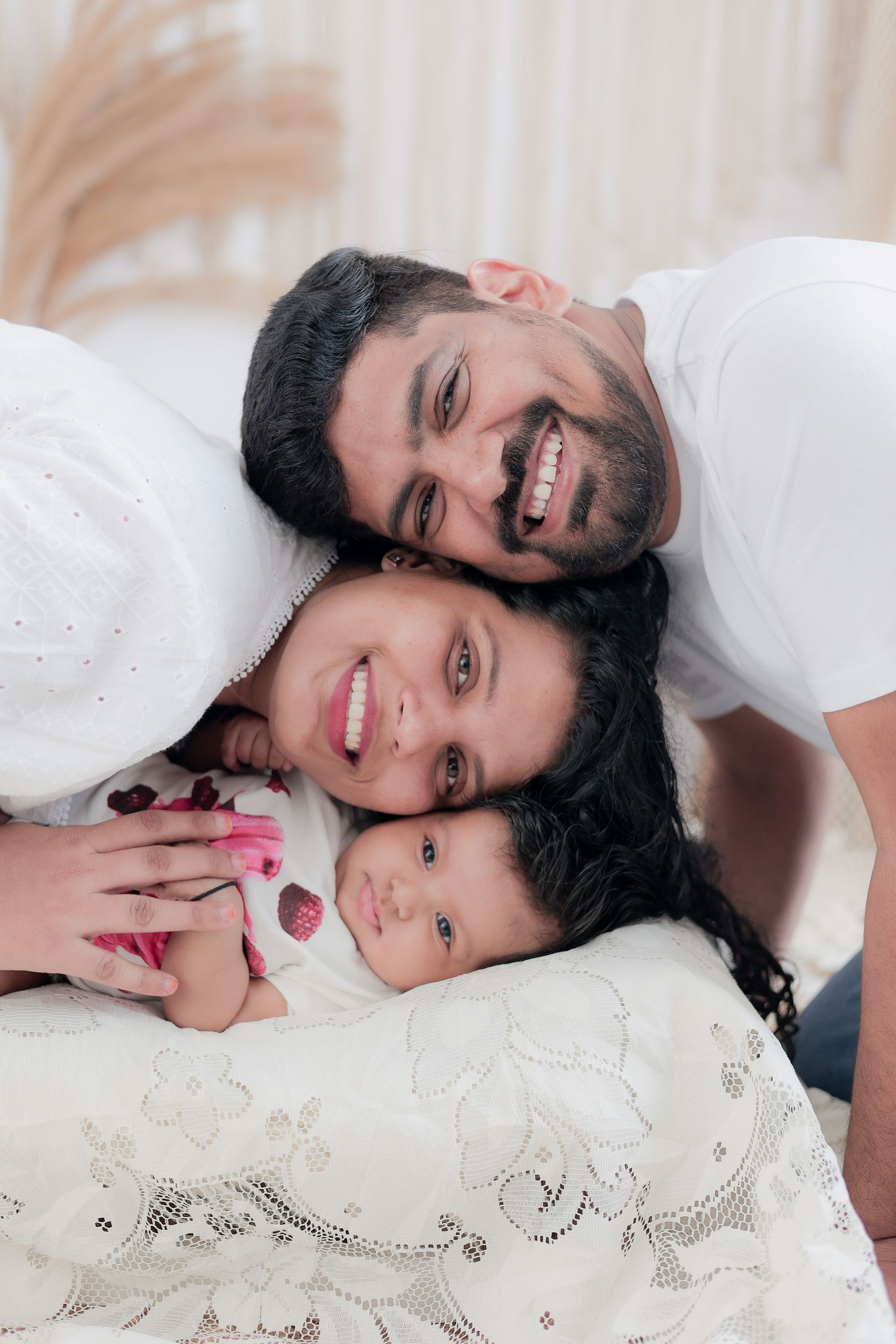 Smiling family of three lying together on a bed, heads close together in a cozy bedroom.
