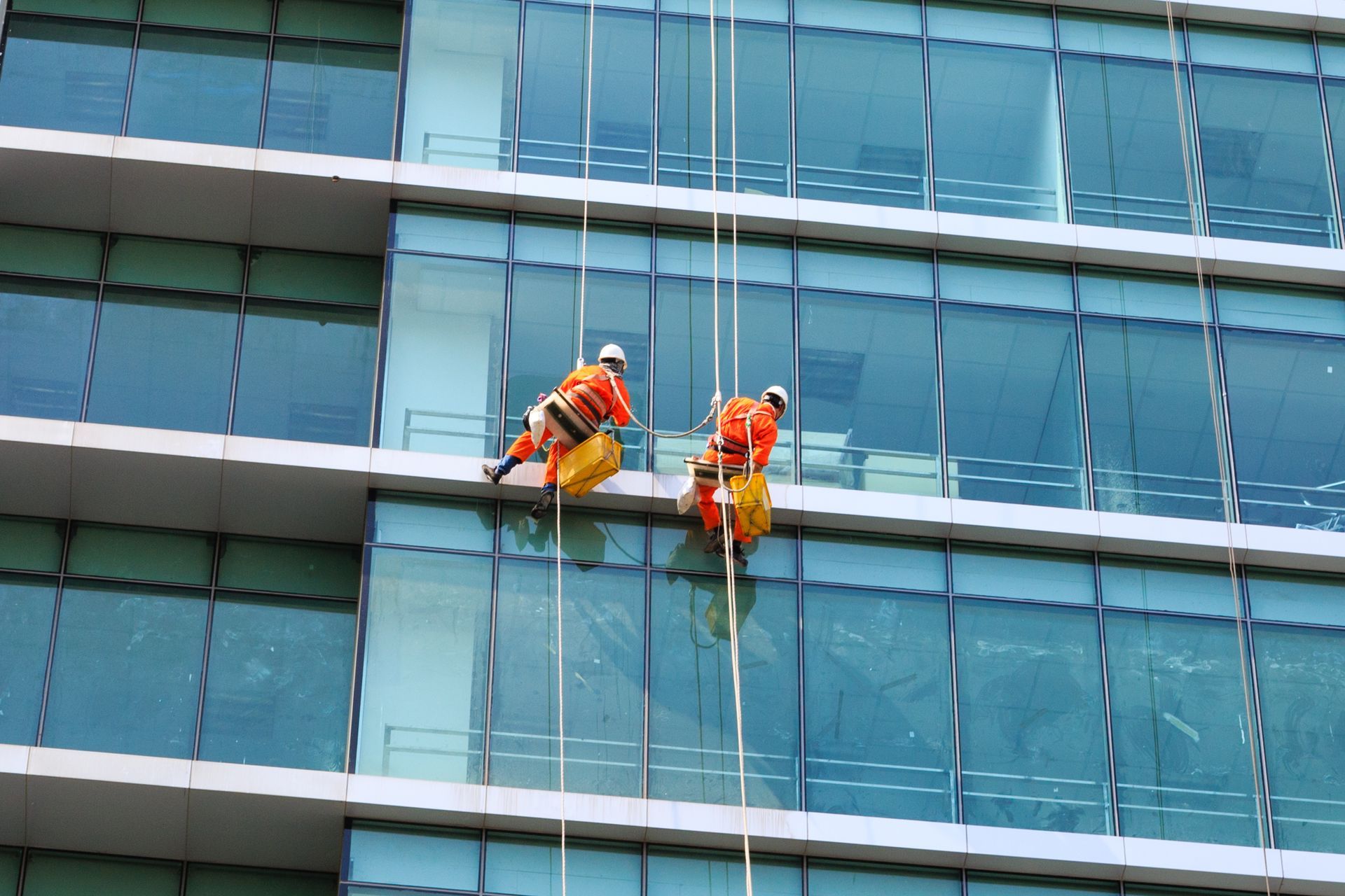 Workers wearing orange uniforms, performing commercial window cleaning service on a tall building.