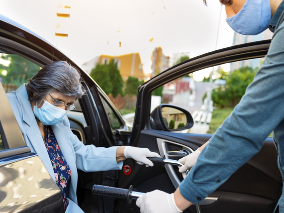 An elderly woman wearing a mask is getting out of a car.
