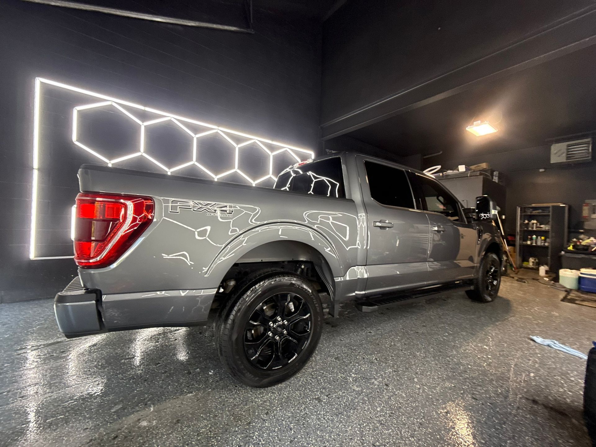 Gray Ford F-150 truck parked inside a garage with black rims and hexagon-shaped neon lights.