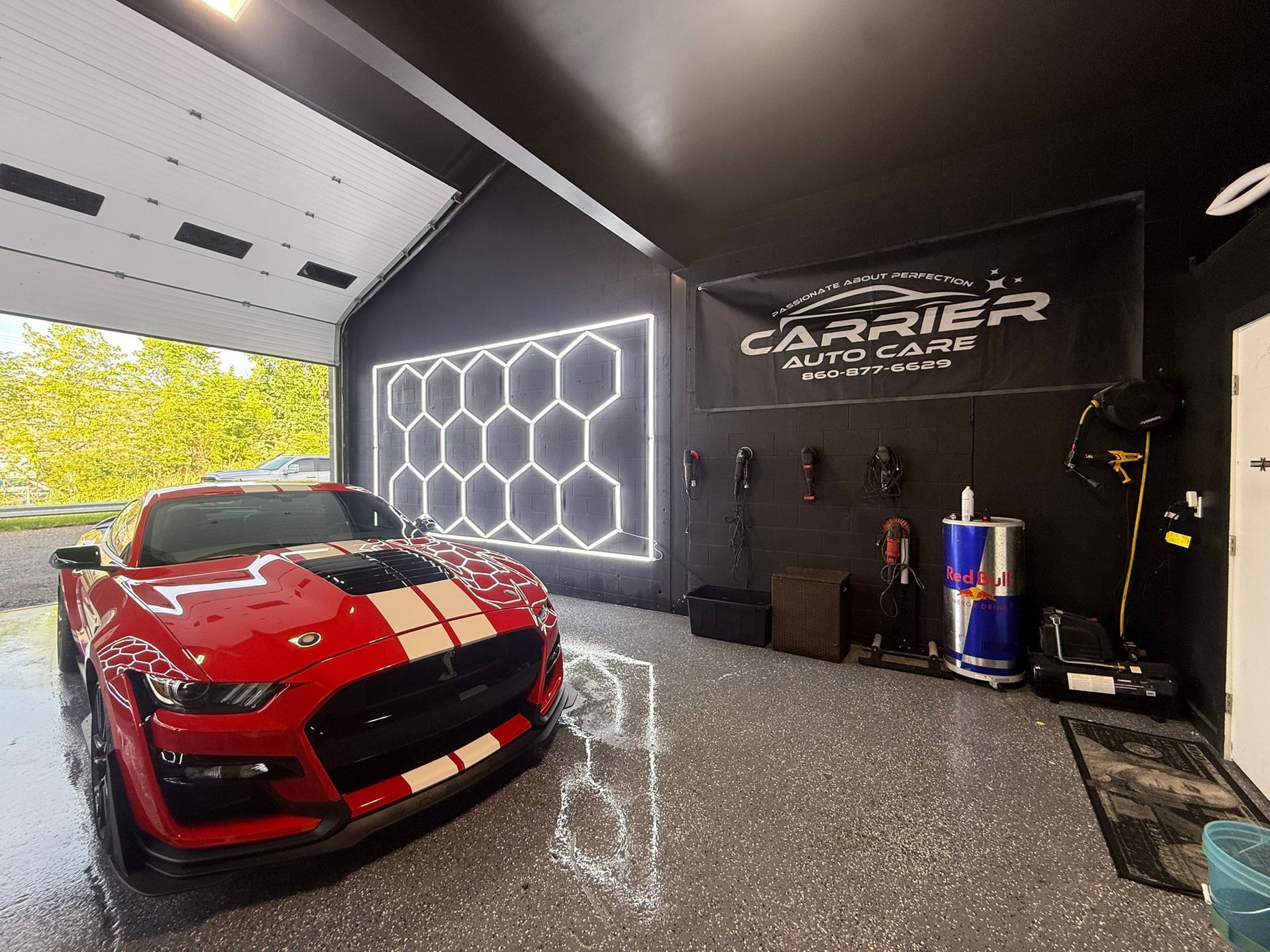 Red Shelby Cobra sports car in a black garage with honeycomb lights; Carrier Auto Care sign.