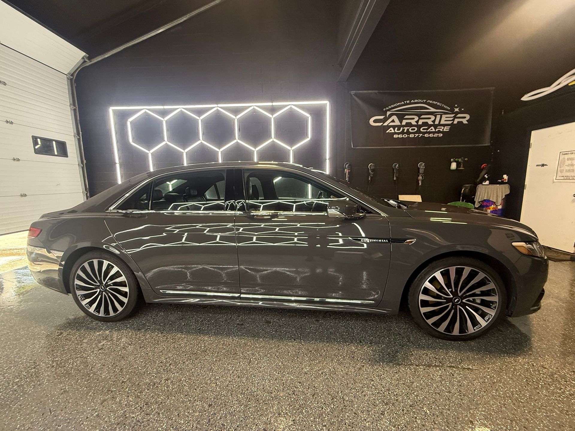Gray Lincoln sedan parked inside a garage; neon honeycomb light fixture on the wall.