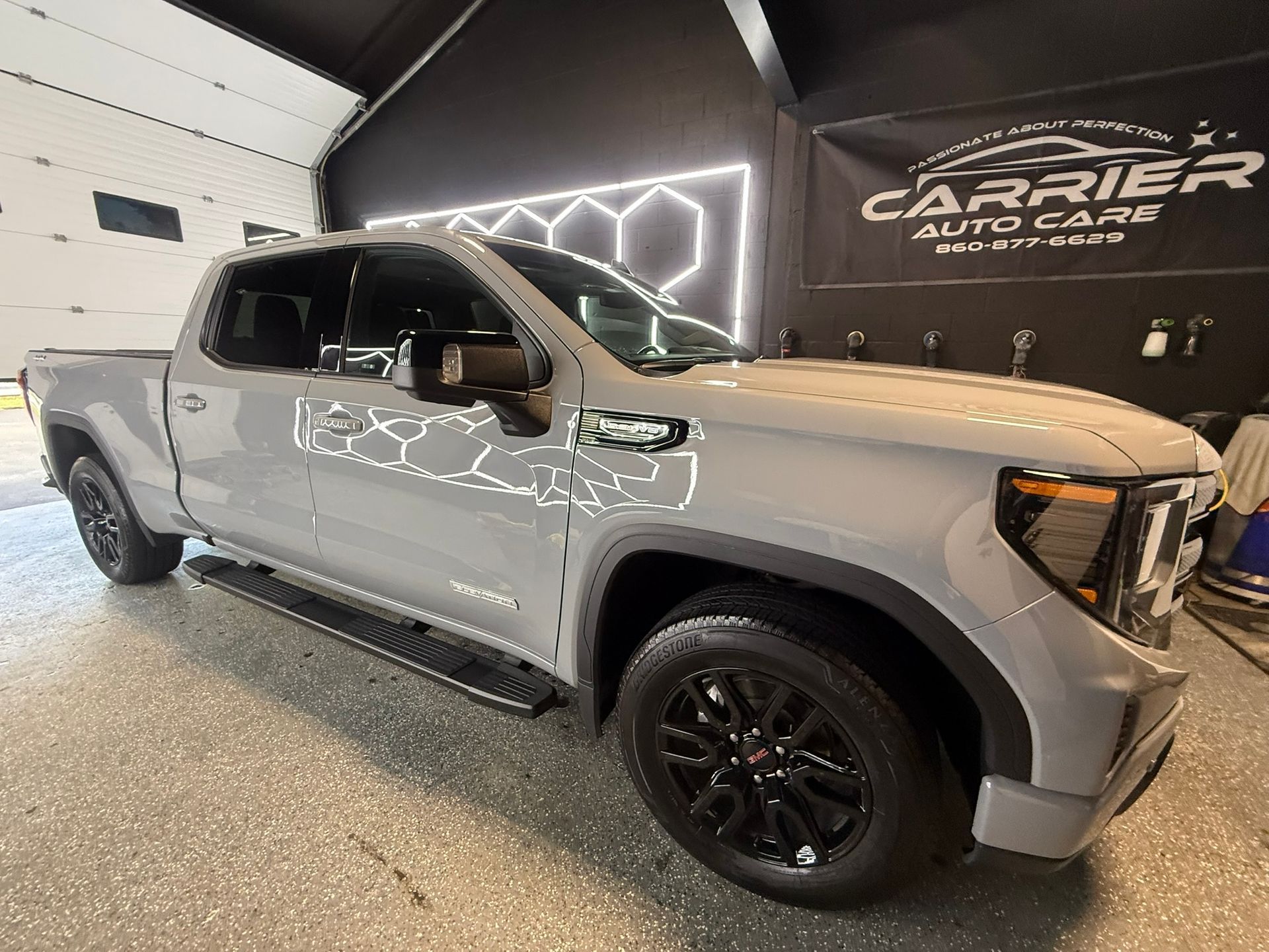 Gray GMC pickup truck parked inside a detailing shop with black wheels, side steps, and banner.