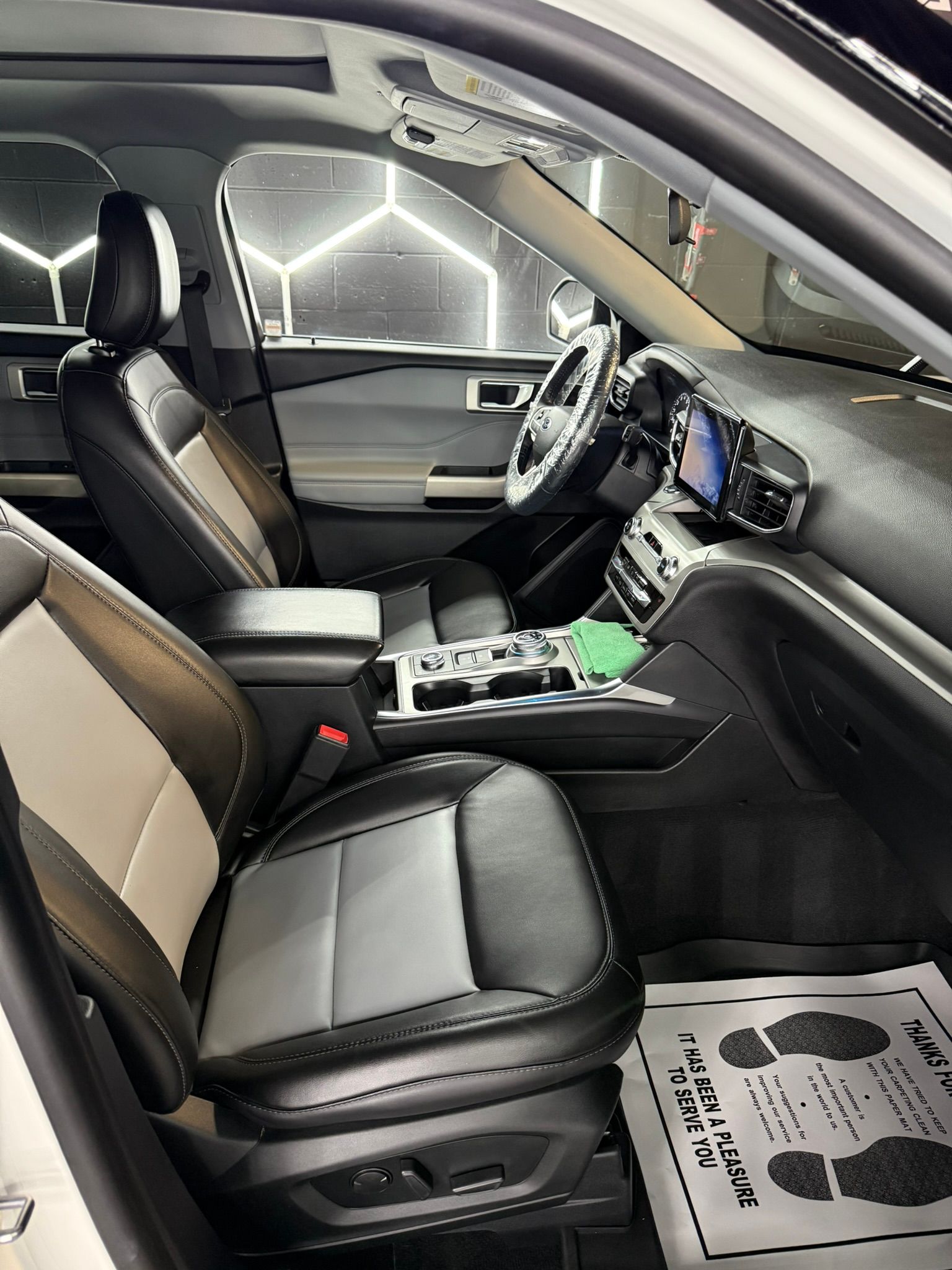 Interior view of a white and black car with leather seats, steering wheel, and dashboard. A paper is on the floor.