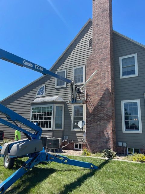 A blue lift near a house with someone working by a brick chimney, and green grass.