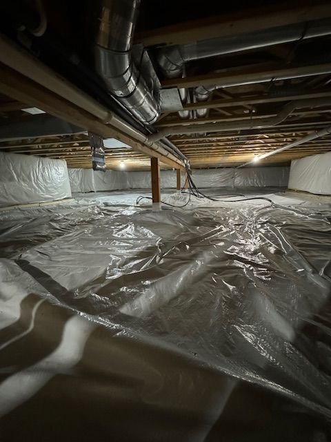 Crawlspace with plastic sheeting on the ground, ductwork and wooden beams overhead.