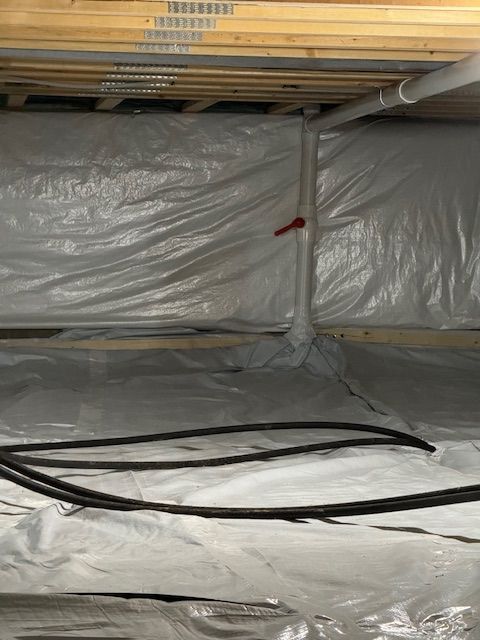 White plastic sheeting lines a crawl space; a vertical white pipe with a red valve extends from the floor.