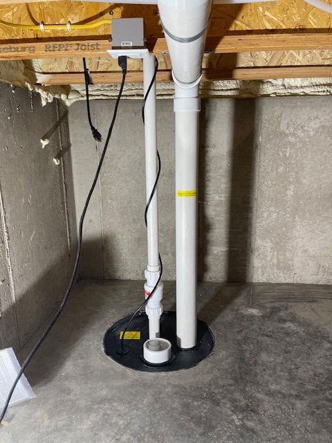 Basement sump pump system with vertical pipes, a black base, and electrical components.