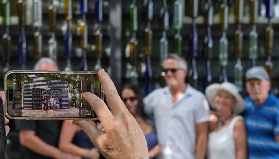 Person holding a smartphone to photograph a group in front of a wall of hanging bottles