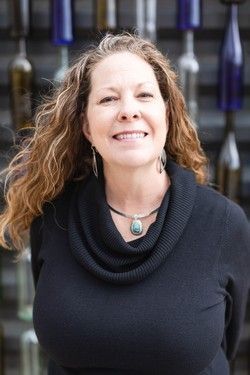 Smiling woman in a black sweater and turquoise necklace standing outdoors in front of blurred railing