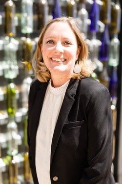 Smiling person in a black blazer standing before a colorful glass wall