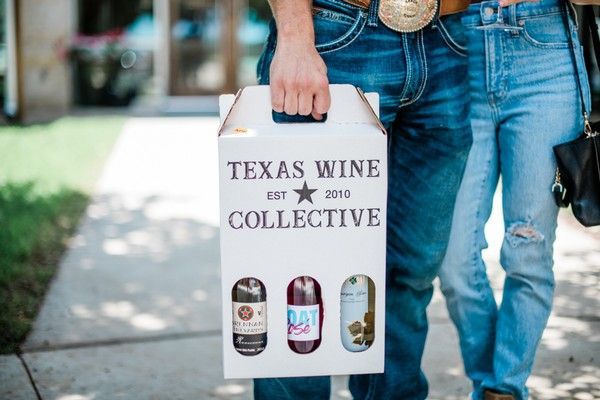 Person holding Texas Wine Collective gift bag with wine bottles, standing outdoors on a sidewalk