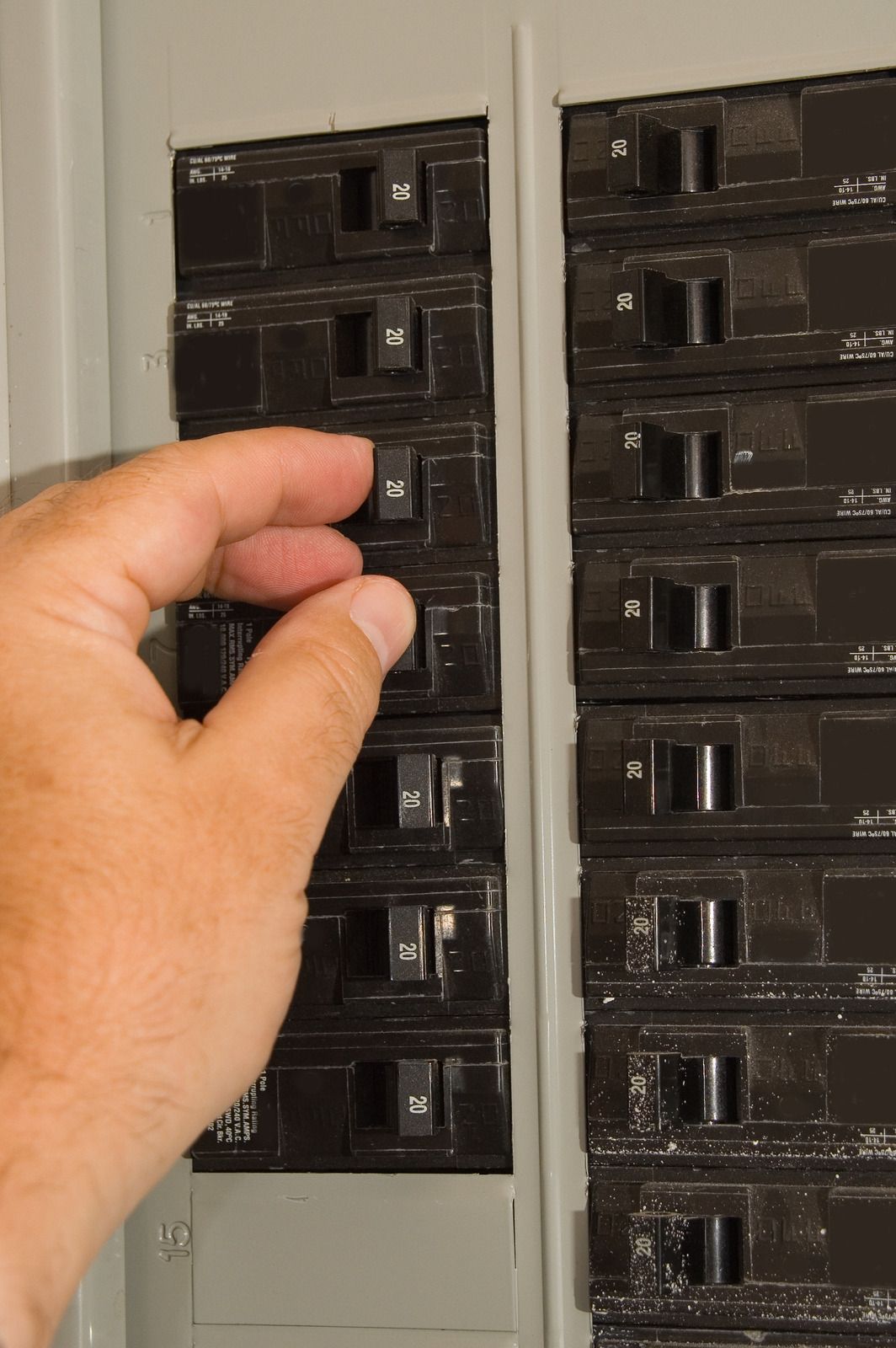 Hand turning off a black breaker switch in an electrical panel