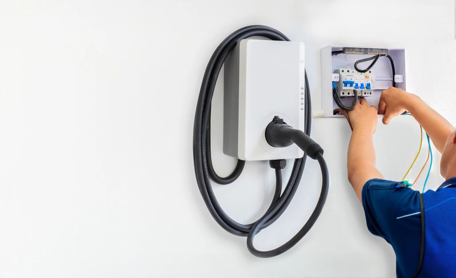 Person installing an electric vehicle charger on a white wall, with electrical box open.