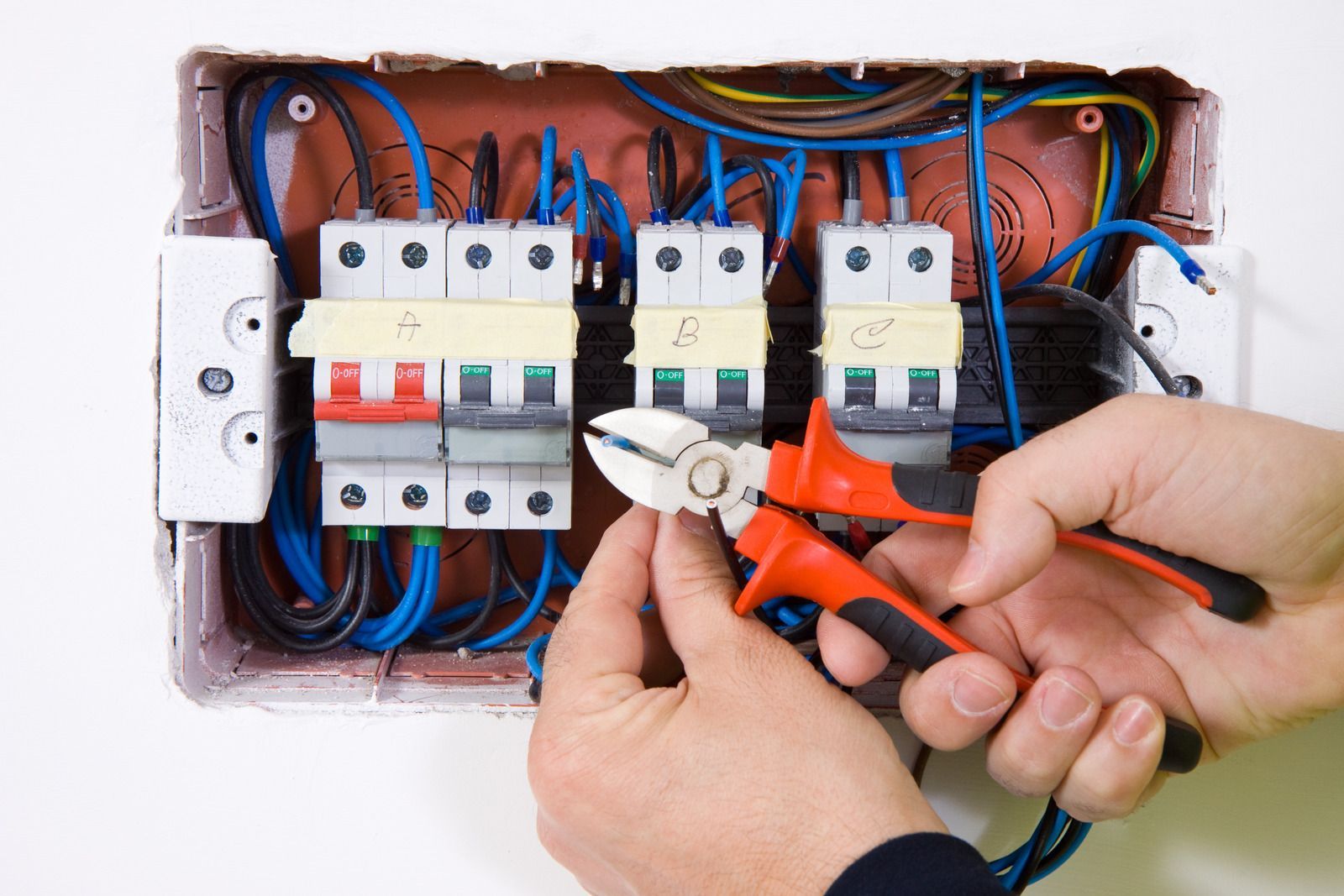 Hands using pliers to wire an electrical breaker panel with red, blue, and white wires