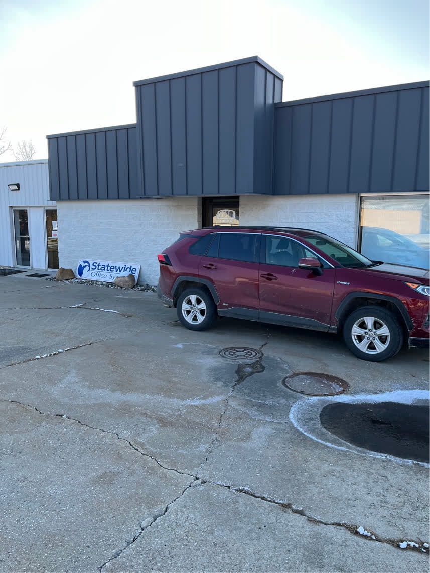 Red SUV parked in front of a white building with a gray roof. Concrete parking area.