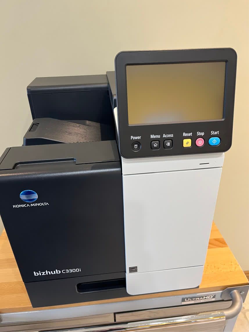 Konica Minolta bizhub printer, black and white, with a touchscreen interface on a wooden surface.