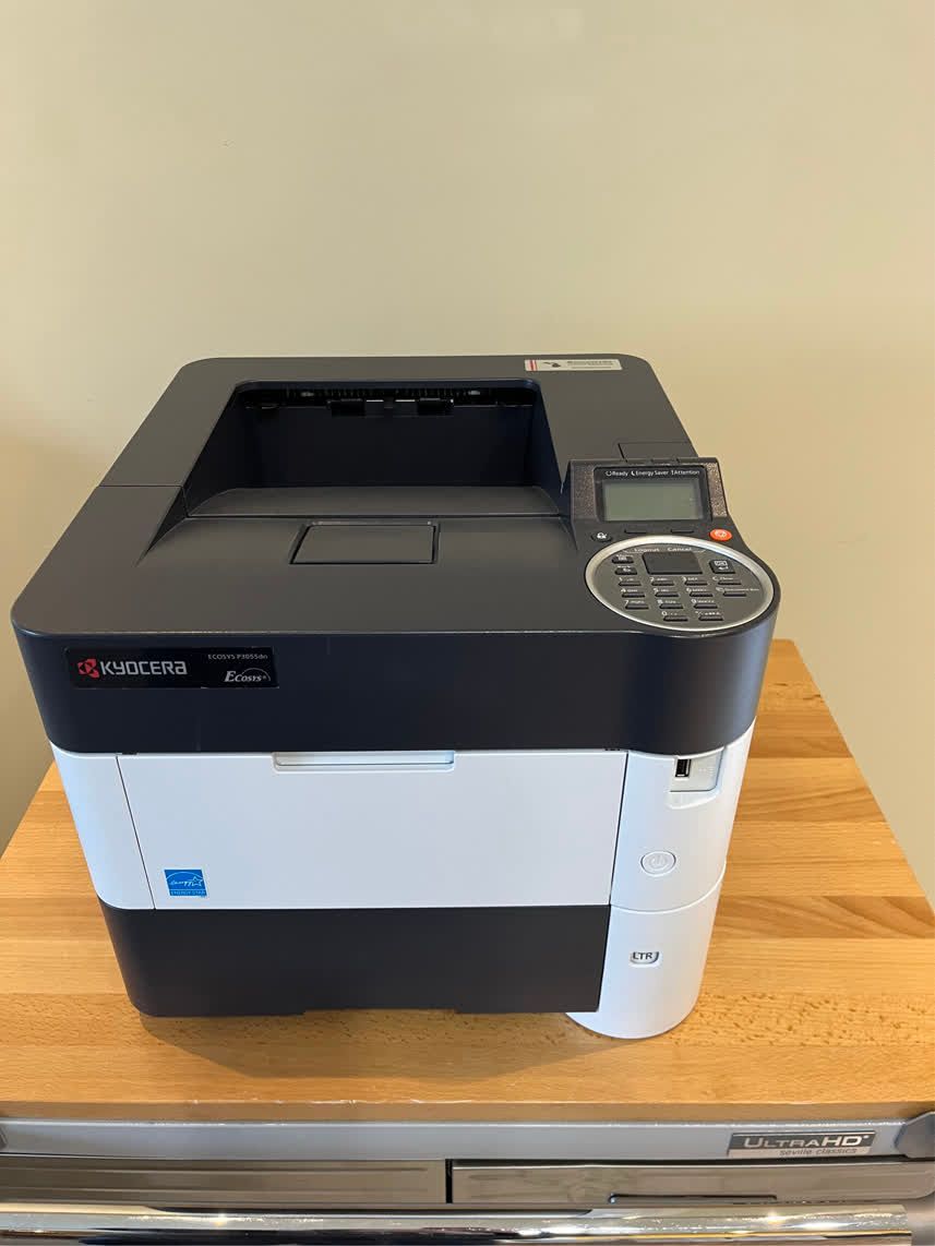Kyocera ECOSYS P6130cdn printer on a wooden surface. Black, white, and gray colors. Control panel on top right.