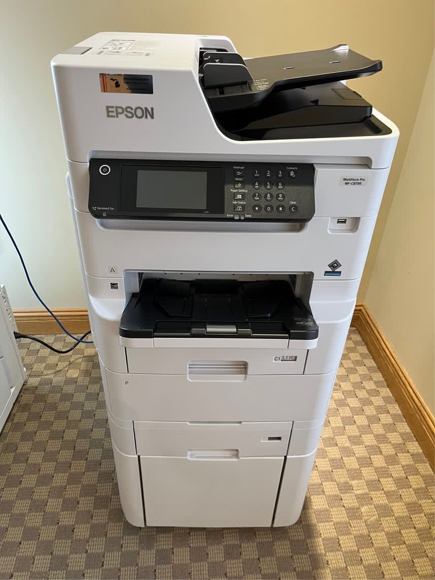 White Epson multi-function printer with control panel, document feeder, and paper trays, indoors.