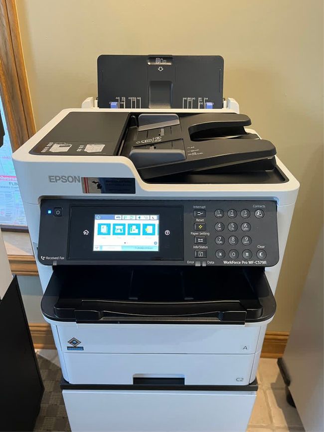 Epson all-in-one printer with touchscreen and paper trays, in a home office setting.