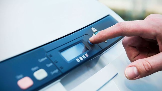 Person's finger pressing a printer button on a blue panel.