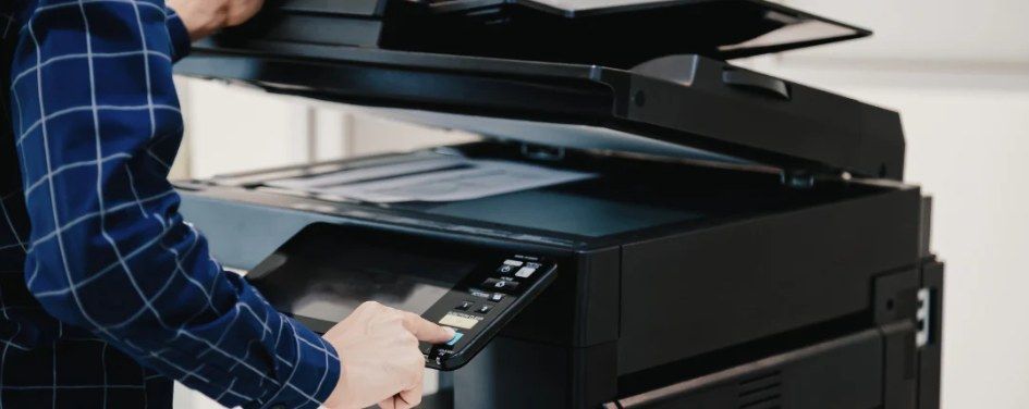 Person operating a black photocopier, pressing buttons.