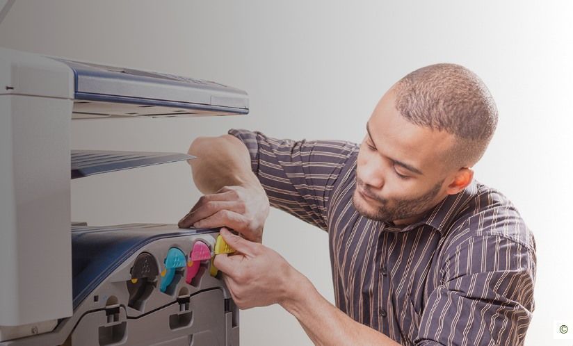 Man servicing a color printer, adjusting ink cartridges.