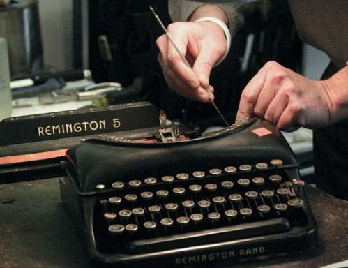 Person repairing a black Remington Rand typewriter with a tool, close-up.