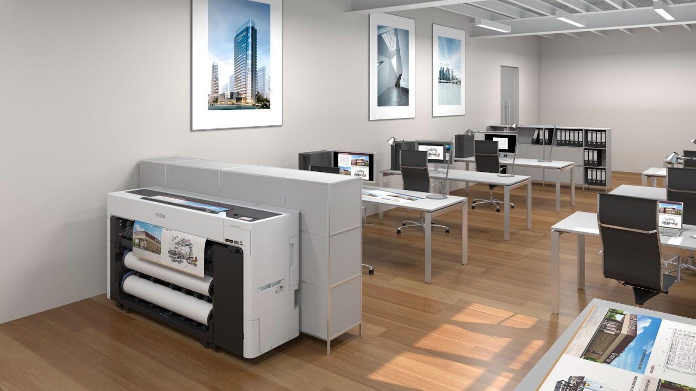 An office with a large printer, desks, computers, and posters on the walls.