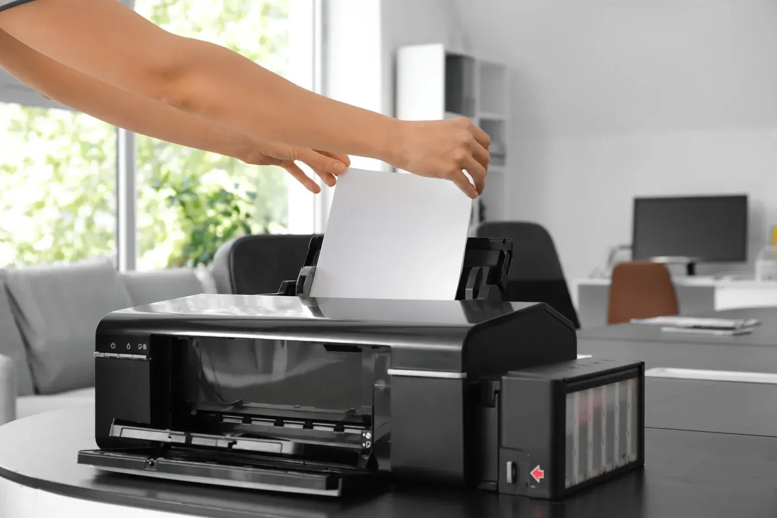 Person loading white paper into a black printer on a table in a home office.