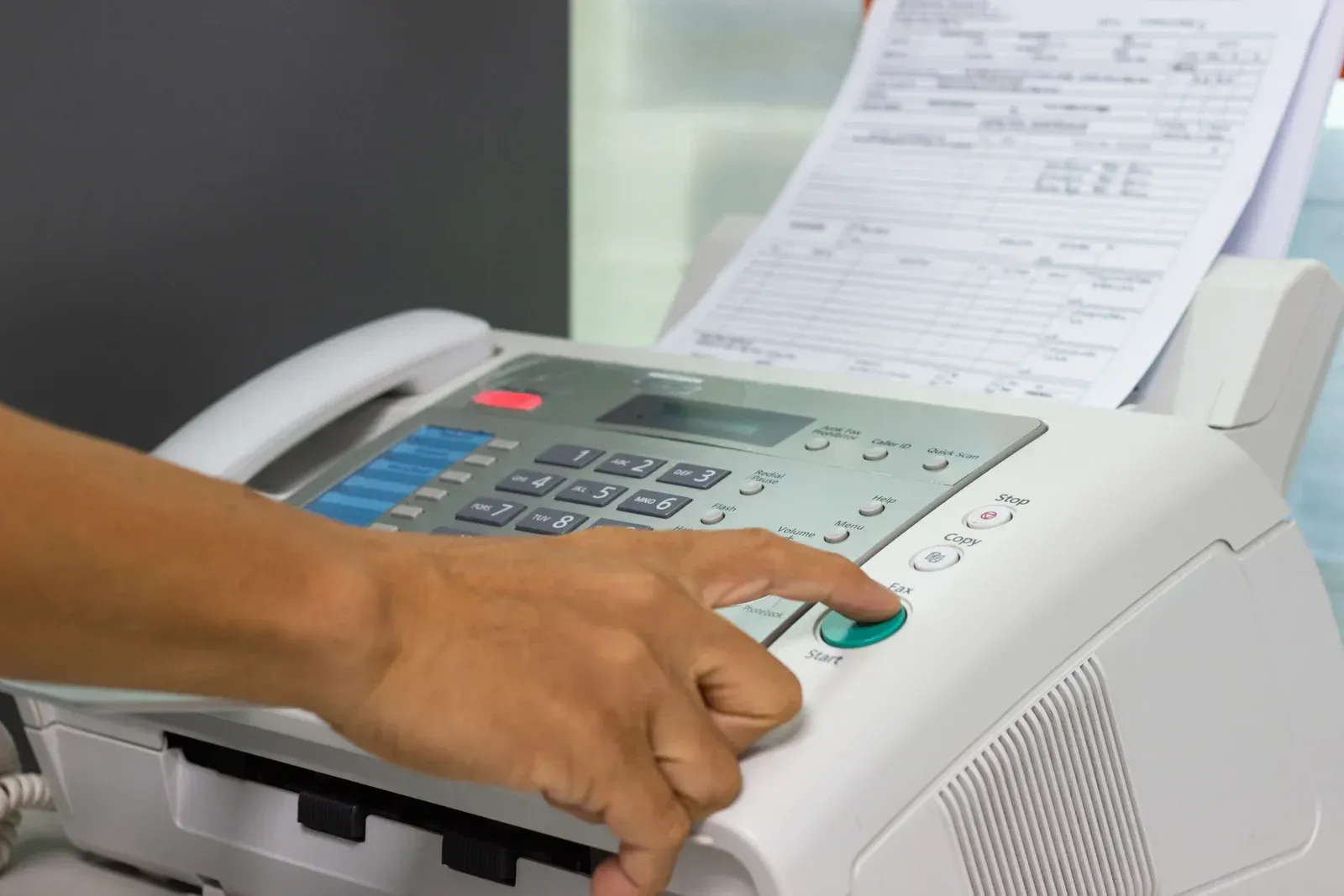Person's hand pressing a button on a fax machine, a document is being fed through.