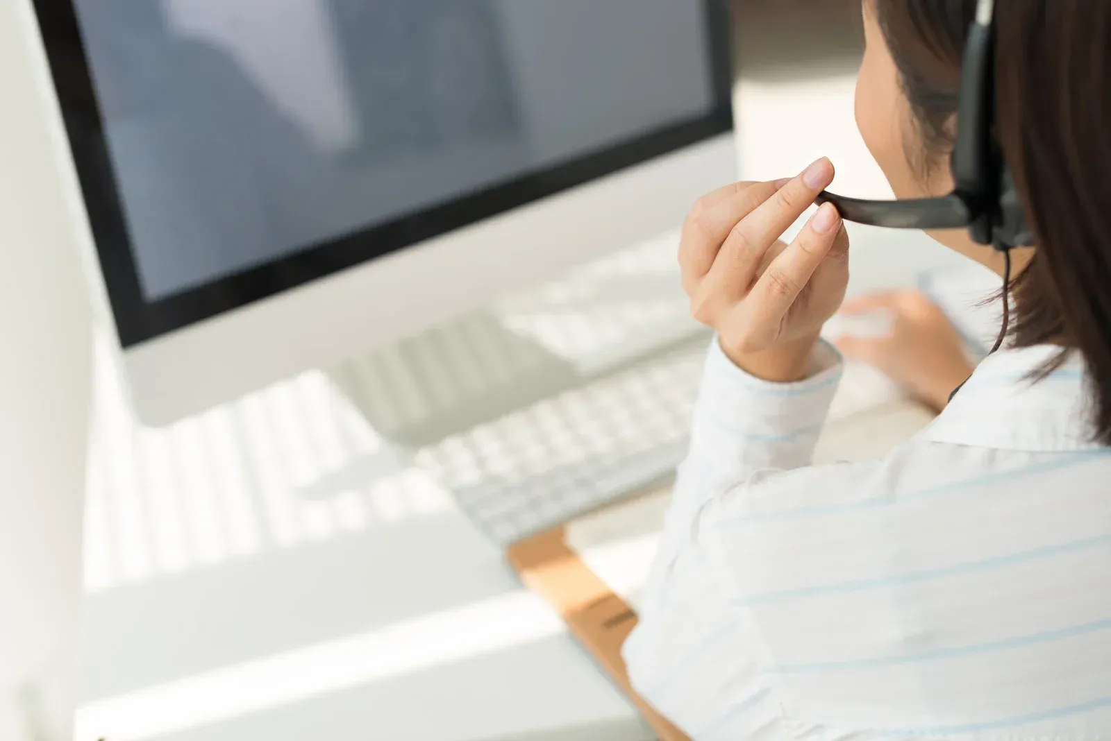 Woman wearing a headset, working at a computer, holding headset microphone.