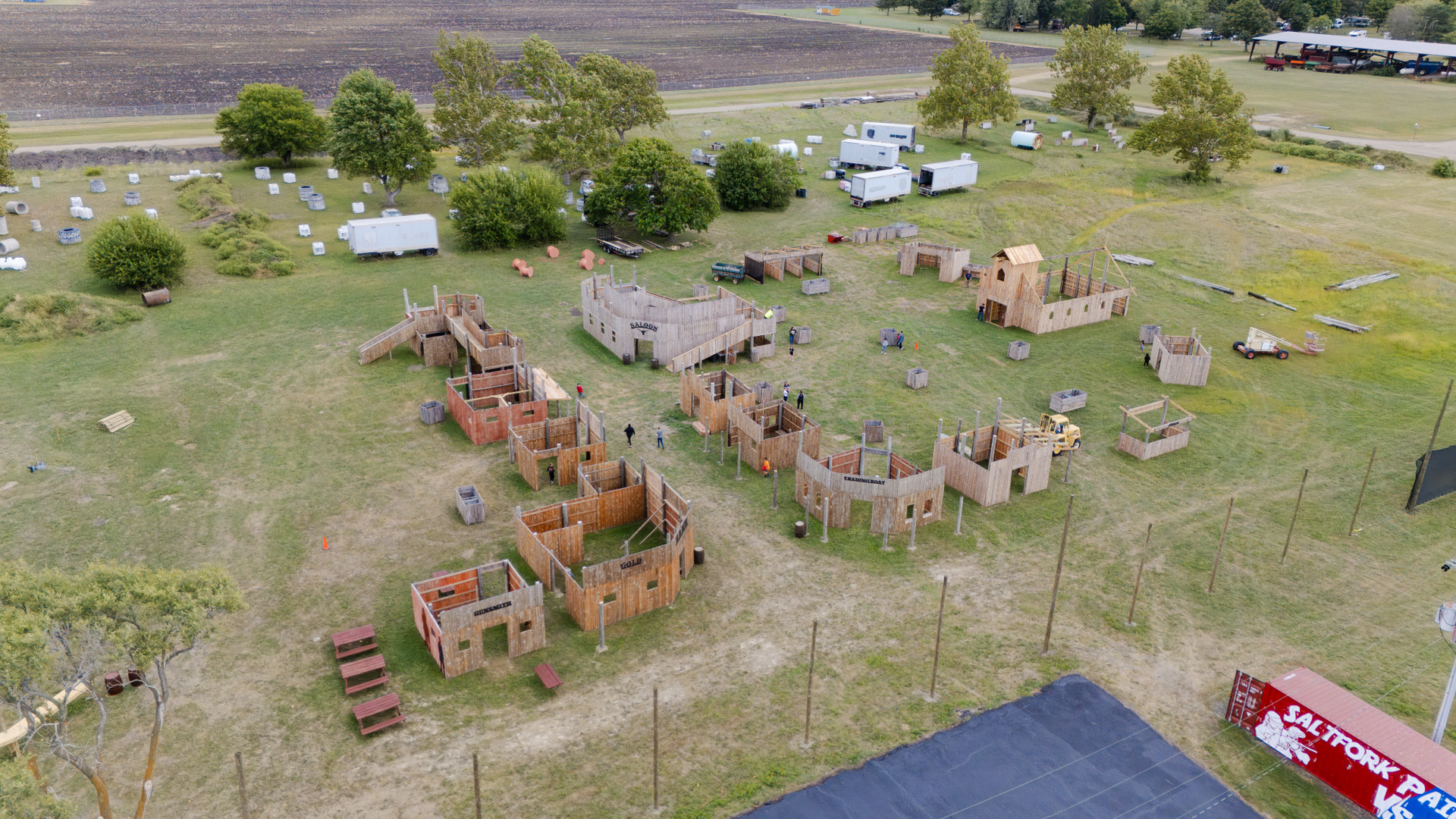Aerial view of a paintball course with wooden structures, trees, and open fields.