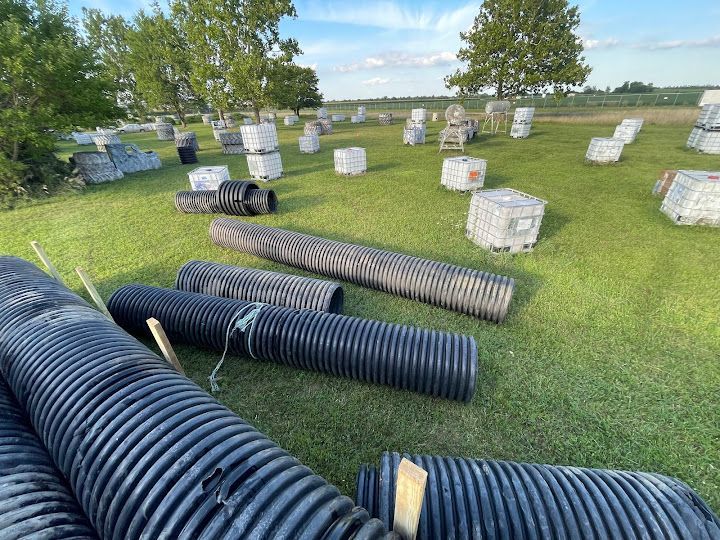 Paintball field with black tubes and concrete bunkers on green grass under blue sky.
