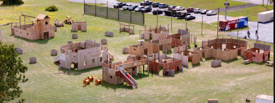 An aerial view of a paintball field with wooden structures and parked cars.