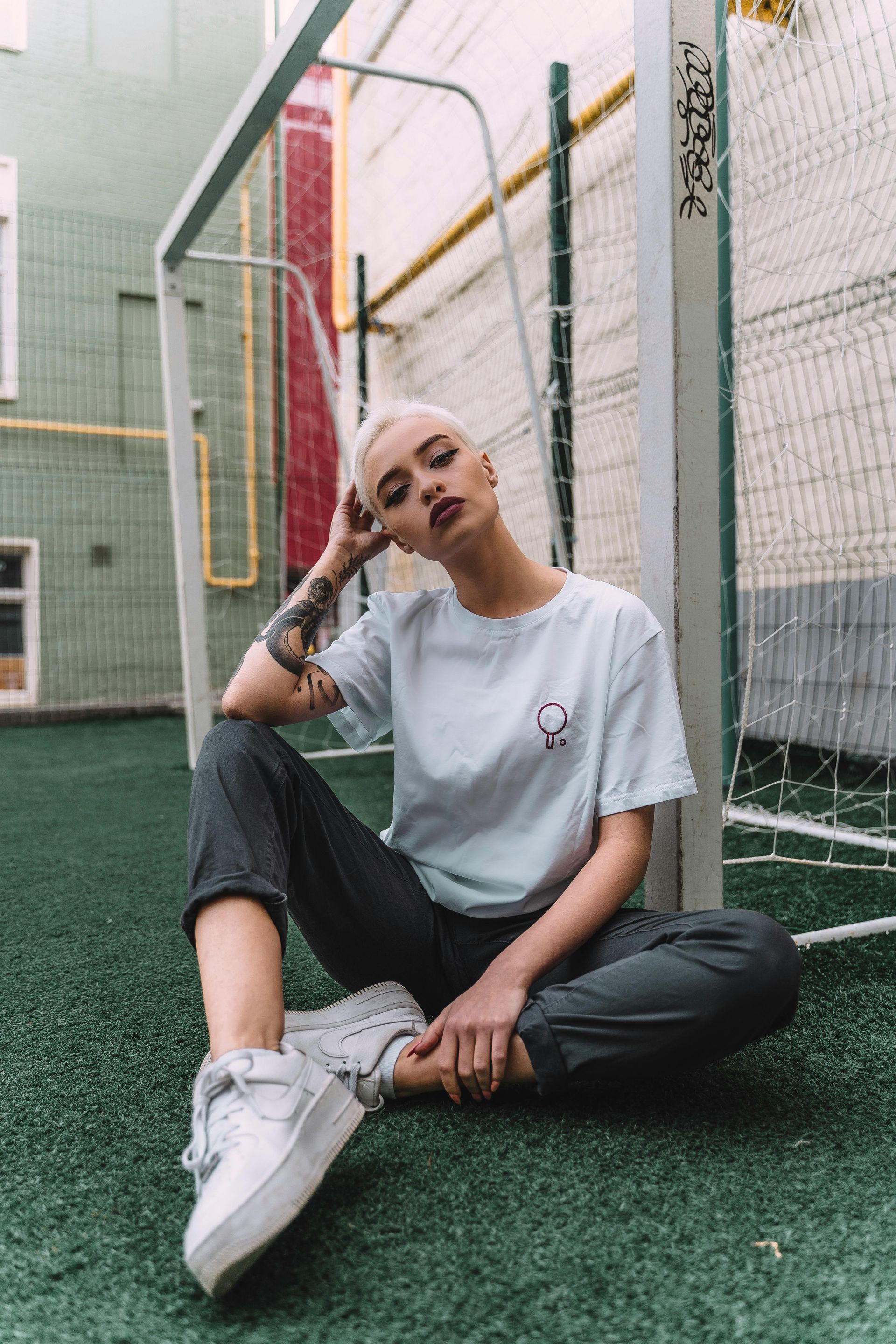 A woman is sitting on the grass in front of a soccer goal.