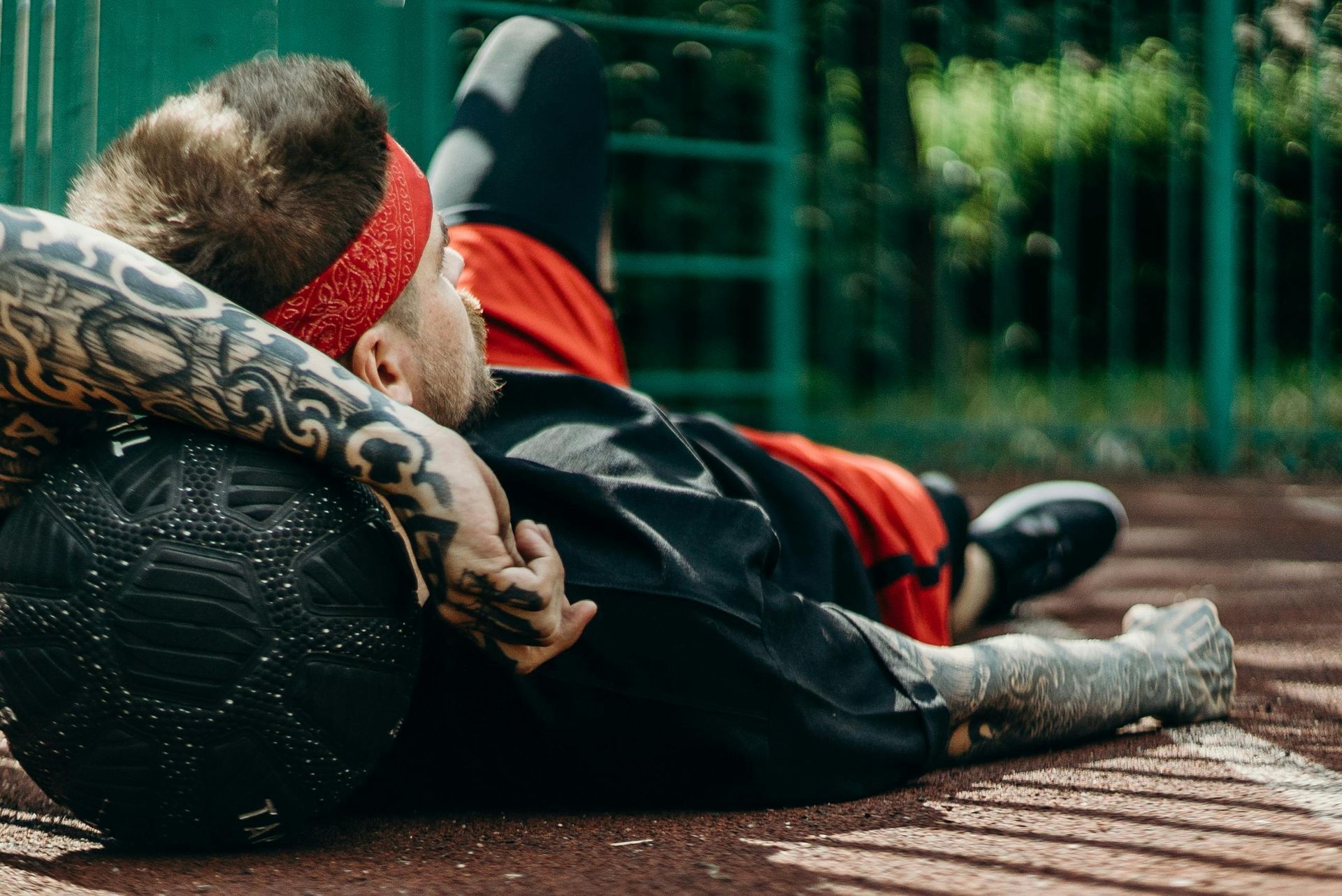 A man with tattoos is laying on the ground with a ball.