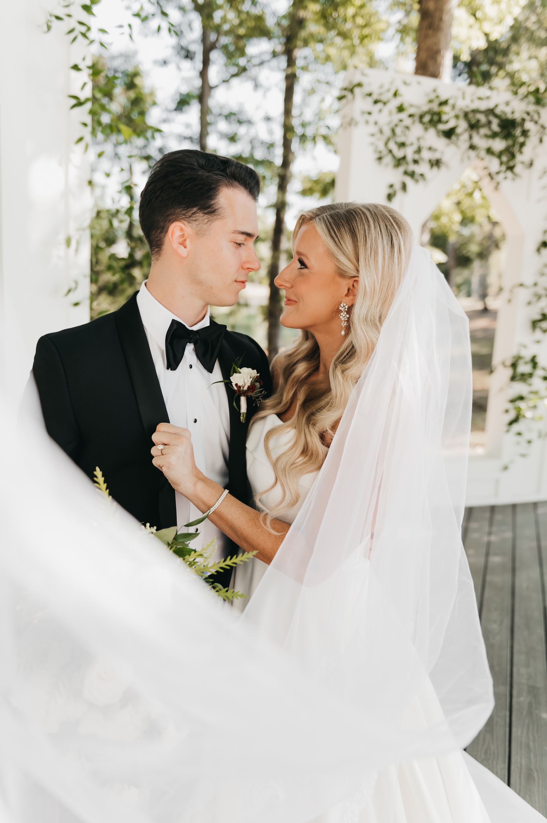Bride and groom looking at each other, outdoors. Bride in white dress, veil; groom in tuxedo.