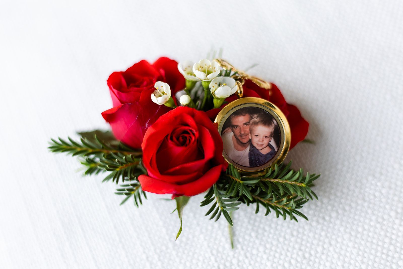 Red rose boutonniere with small framed photo of two people.
