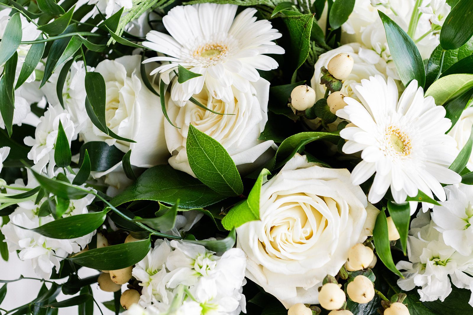 White floral bouquet with roses, daisies, and greenery.