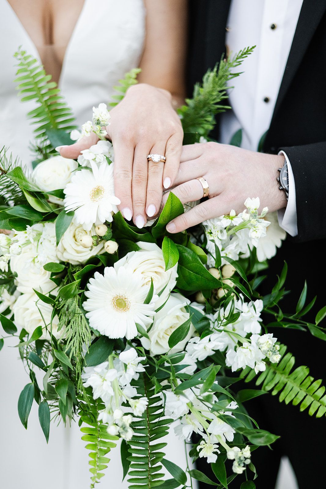 Hands of a couple, with rings, on a white floral bouquet.