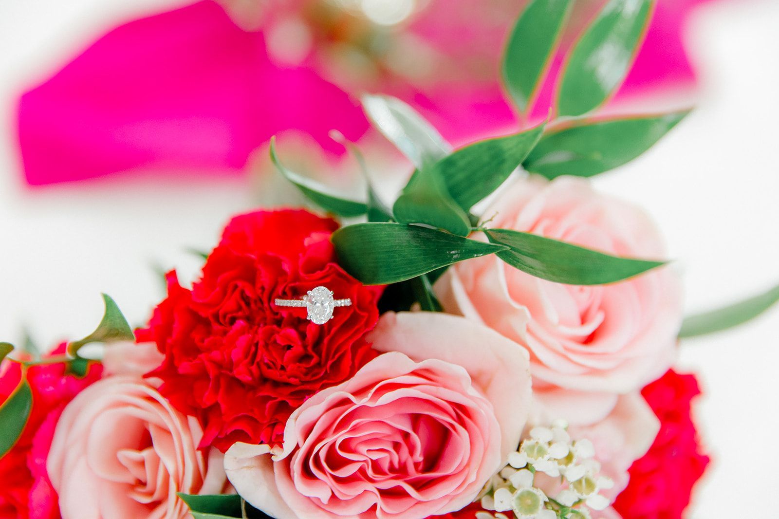 Engagement ring on a bouquet of red and pink roses with green leaves.