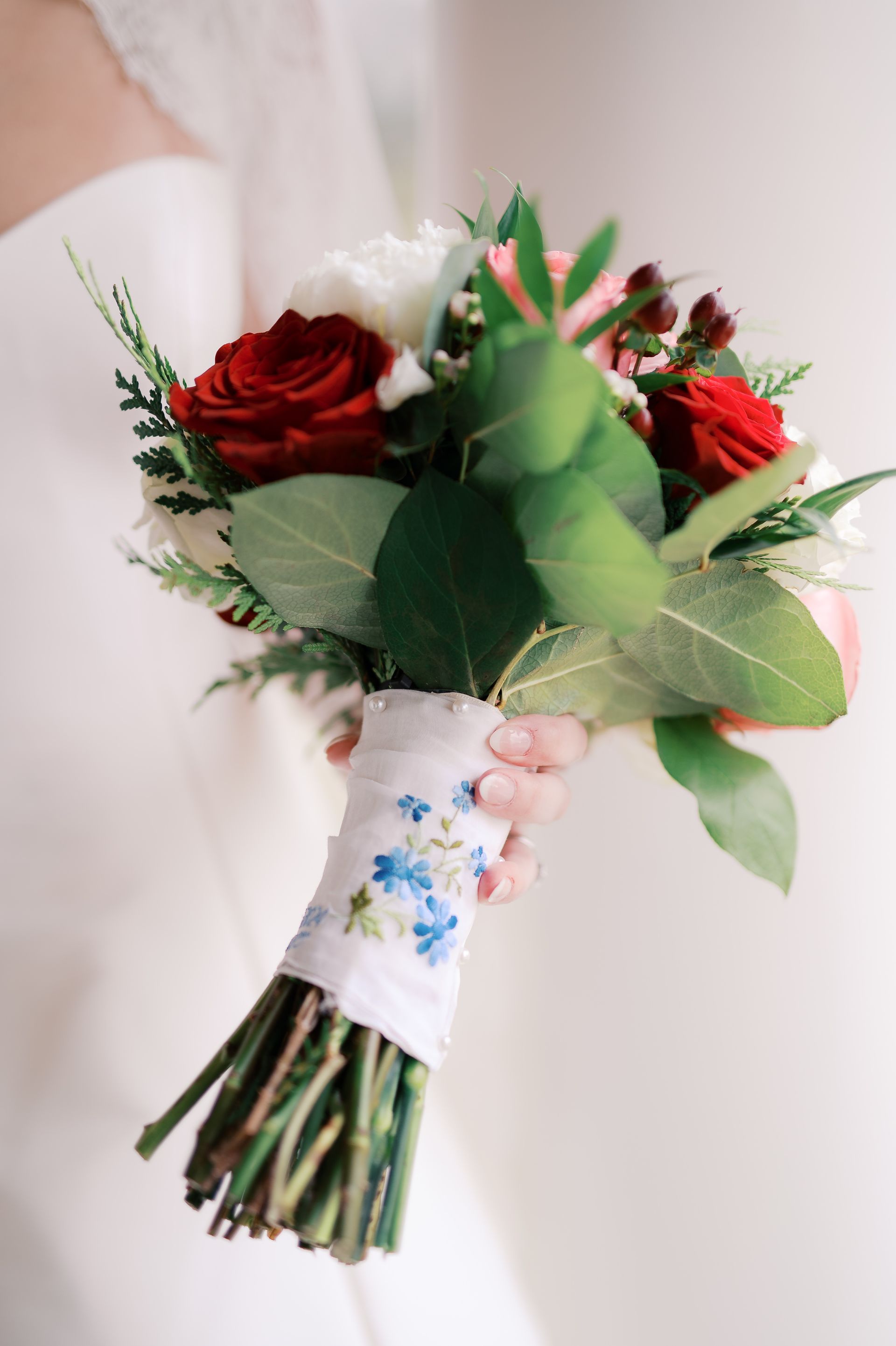 Bride holding a bouquet of red and white flowers wrapped in a blue floral ribbon.